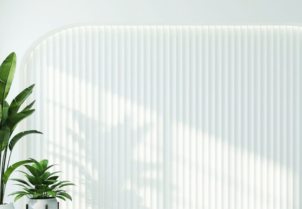 Minimalist white wall with vertical ridges, featuring two green potted plants in the lower left corner and sunlight casting soft shadows across the surface.