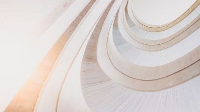 Curved, modern staircase with light-colored concrete, viewed from below, creating a pattern of repeating arches and geometric shapes.