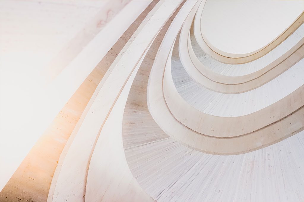 Curved, modern staircase with light-colored concrete, viewed from below, creating a pattern of repeating arches and geometric shapes.